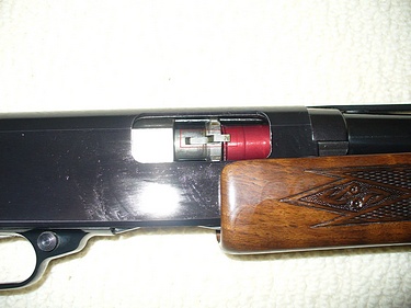 shotgun, action partially open with dummy round hooked on extractor